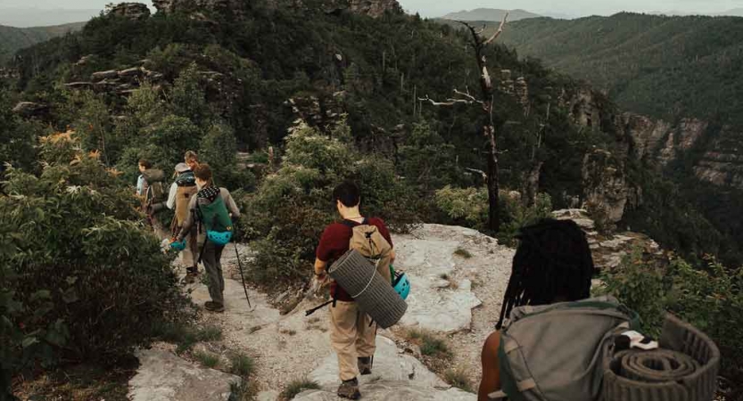 a group of teens wearing backpacks and hiking gear navigate a trail on a backpacking course with outward bound